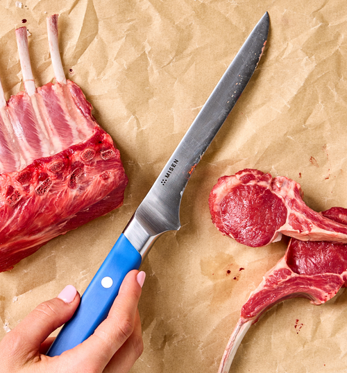 Misen boning knife with blue handle cutting rack of lamb chops on parchment paper