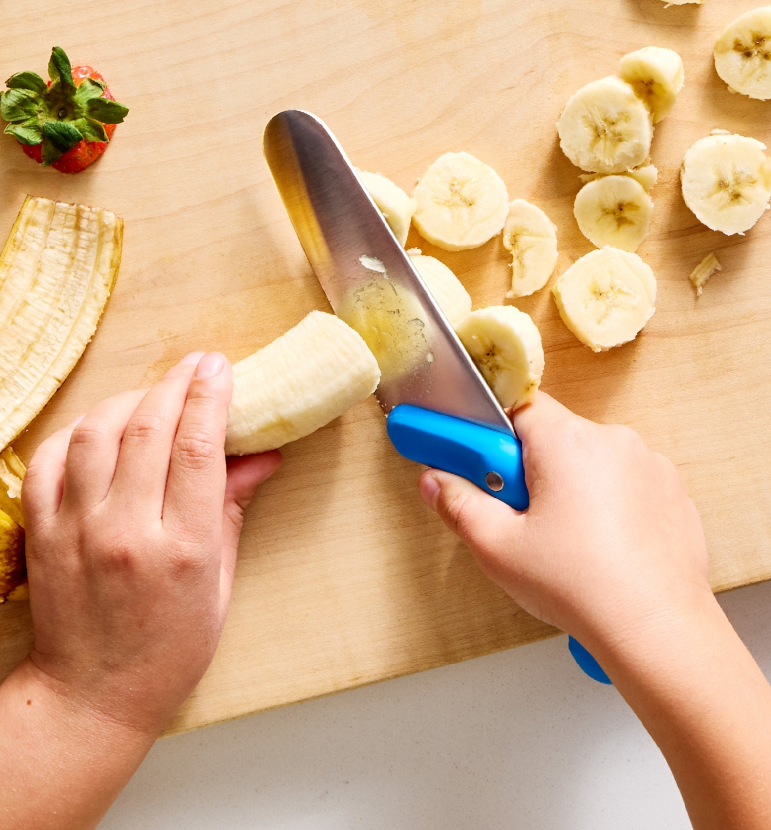 Child slicing banana with kid-safe knife on wooden cutting board