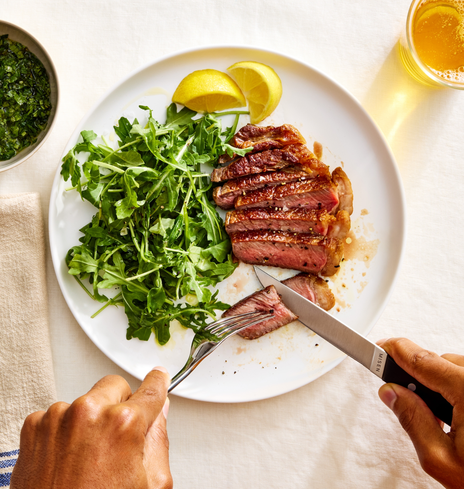 Sliced medium-rare steak with arugula salad and lemon wedges on white plate, cut with Misen steak knife