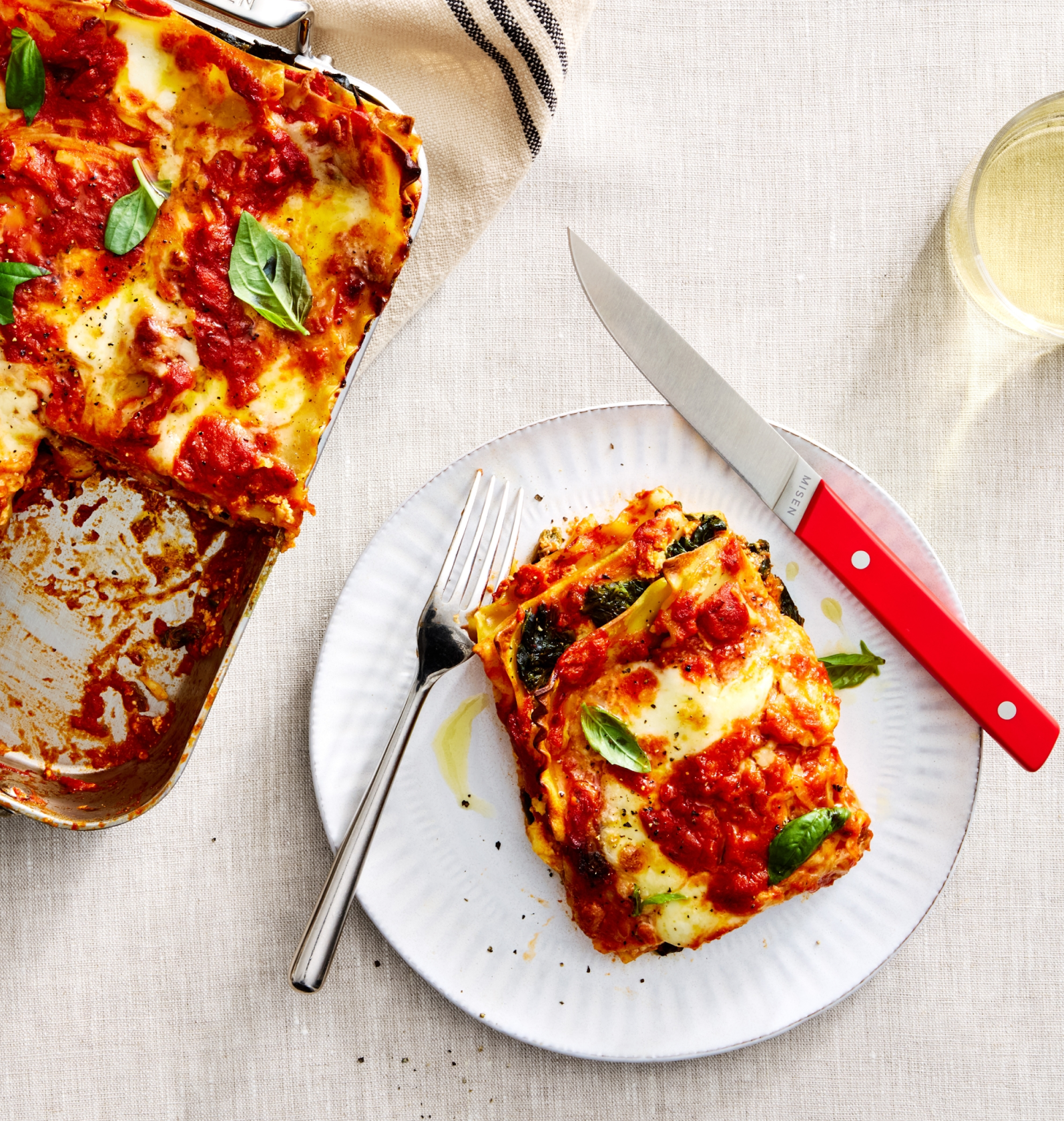 Homemade vegetarian lasagna slice on white plate with tomato sauce, melted mozzarella, and fresh basil