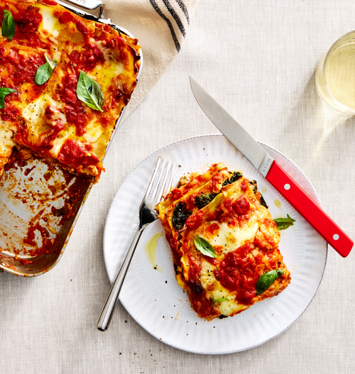 Homemade vegetarian lasagna slice on white plate with tomato sauce, melted mozzarella, and fresh basil